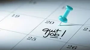A close-up of a calendar with a blue pushpin marking a date and the handwritten words quit job! written on that day.