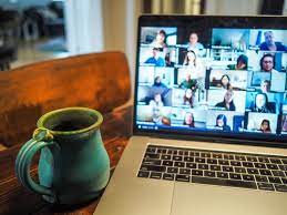 A close-up shot focuses on a laptop screen displaying a large group video call on Zoom with numerous participants.