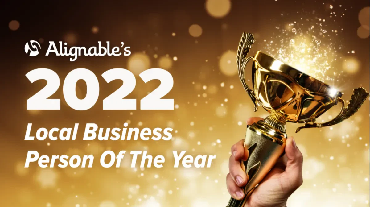 A hand holding up a golden trophy against a sparkling bokeh background, featuring the text Alignable's 2022 Local Business Person Of The Year.