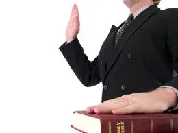 A man in a suit and tie holds a Bible, taking an oath.