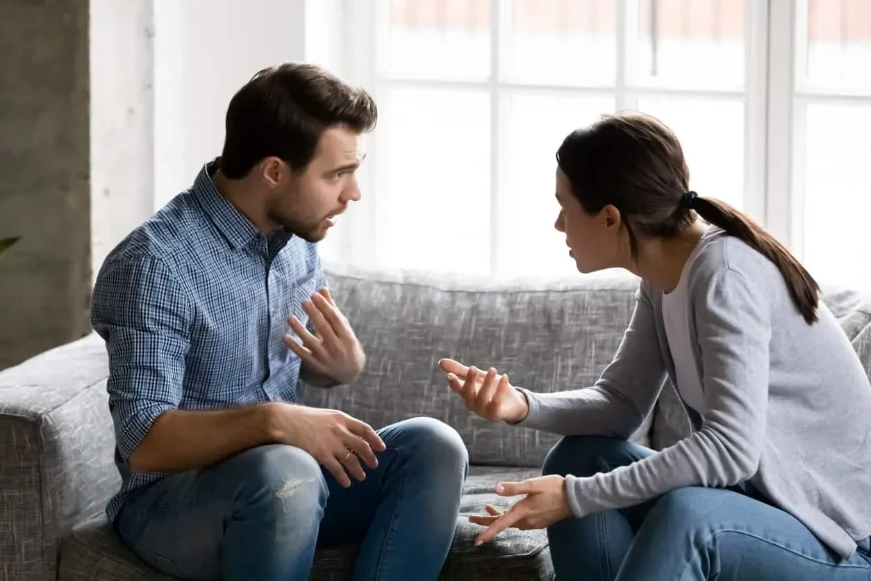 A man and woman are engaged in a heated argument while sitting on a couch in a living room setting.