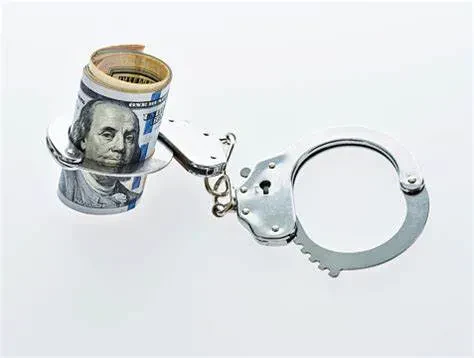 A roll of U.S. hundred-dollar bills is secured in one side of a pair of handcuffs, symbolizing financial crime or the concept of money being restricted or controlled.