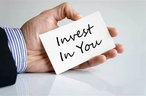 A hand holding a card that says Invest In You in black handwriting.