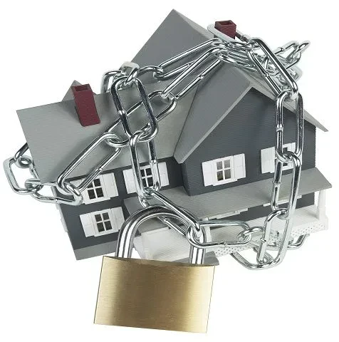 A model of a grey two-story house wrapped securely in thick metallic chains and locked with a large brass padlock in the foreground.