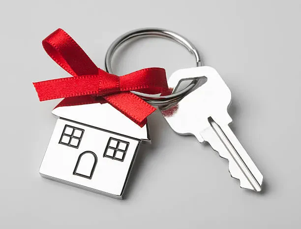 A keychain featuring a house-shaped key adorned with a red ribbon, symbolizing home and warmth.
