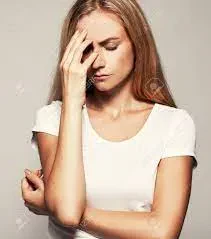 A stressed woman with long brown hair wearing a white shirt, holding her forehead with her hand and closing her eyes in frustration.