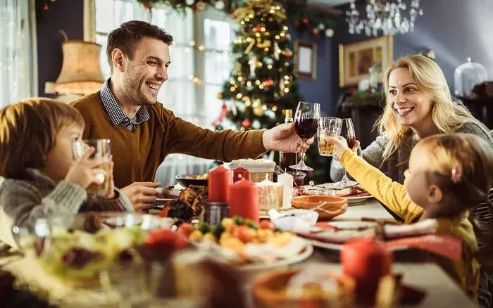 A family gathered around a Christmas table, raising glasses in a toast, surrounded by festive decorations and a holiday feast.