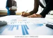 A group of business professionals collaborating on a business plan at a conference table with laptops and documents.