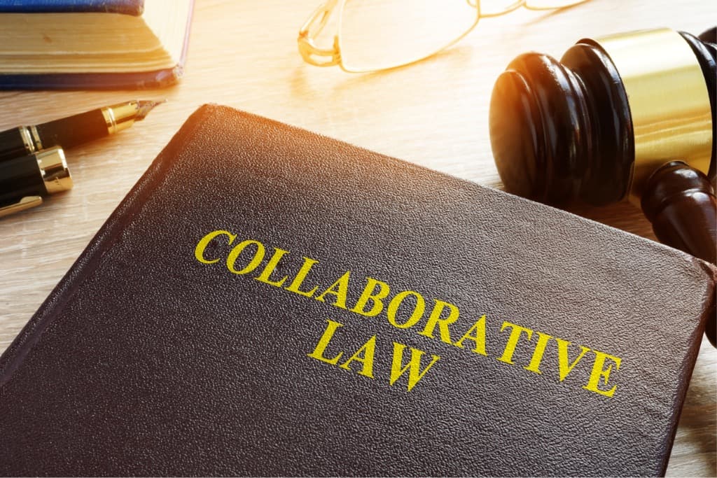 A book titled Collaborative Law sits on a desk next to a gavel, a pen, a pair of glasses, and a closed book.