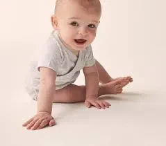 A baby sitting on the floor, smiling, against a plain white background.