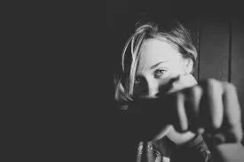 Dramatic black and white close-up portrait of a woman looking directly into the camera with her fist extended toward the foreground in a punching motion against a dark background.