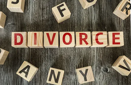 Wooden blocks on a wooden surface spell out DIVORCE in red letters, with other random lettered blocks scattered around.