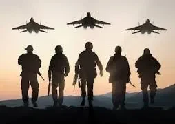 Silhouette of soldiers standing in formation before military jets on an airfield at sunset.