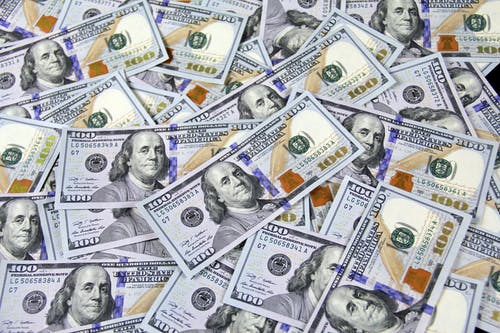 A scattered pile of U.S. one hundred dollar bills, featuring Benjamin Franklin’s portrait, creating a pattern of overlapping currency.