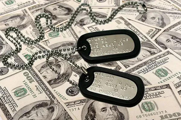A pair of metal military dog tags with black rubber silencers and a ball chain rests on a scattered pile of United States one-hundred-dollar bills.