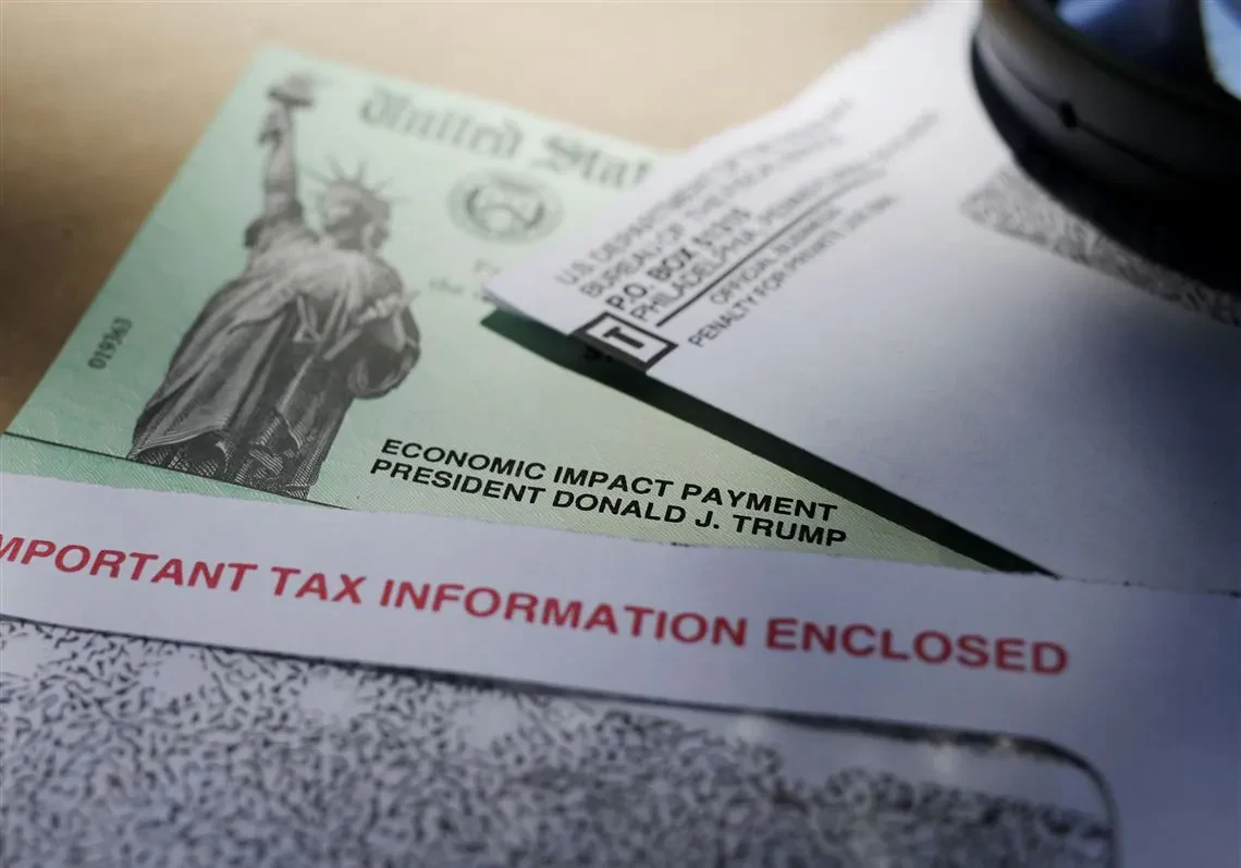 A close-up shot of a green United States Treasury check featuring the Statue of Liberty, with the text "ECONOMIC IMPACT PAYMENT" and "PRESIDENT DONALD J. TRUMP" printed on the front, sitting partially inside a window envelope that reads "IMPORTANT TAX INFORMATION ENCLOSED"