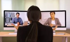 A woman seated at a desk, working on two computers positioned side by side.