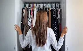 A woman stands in front of a closet, browsing through an assortment of clothes.