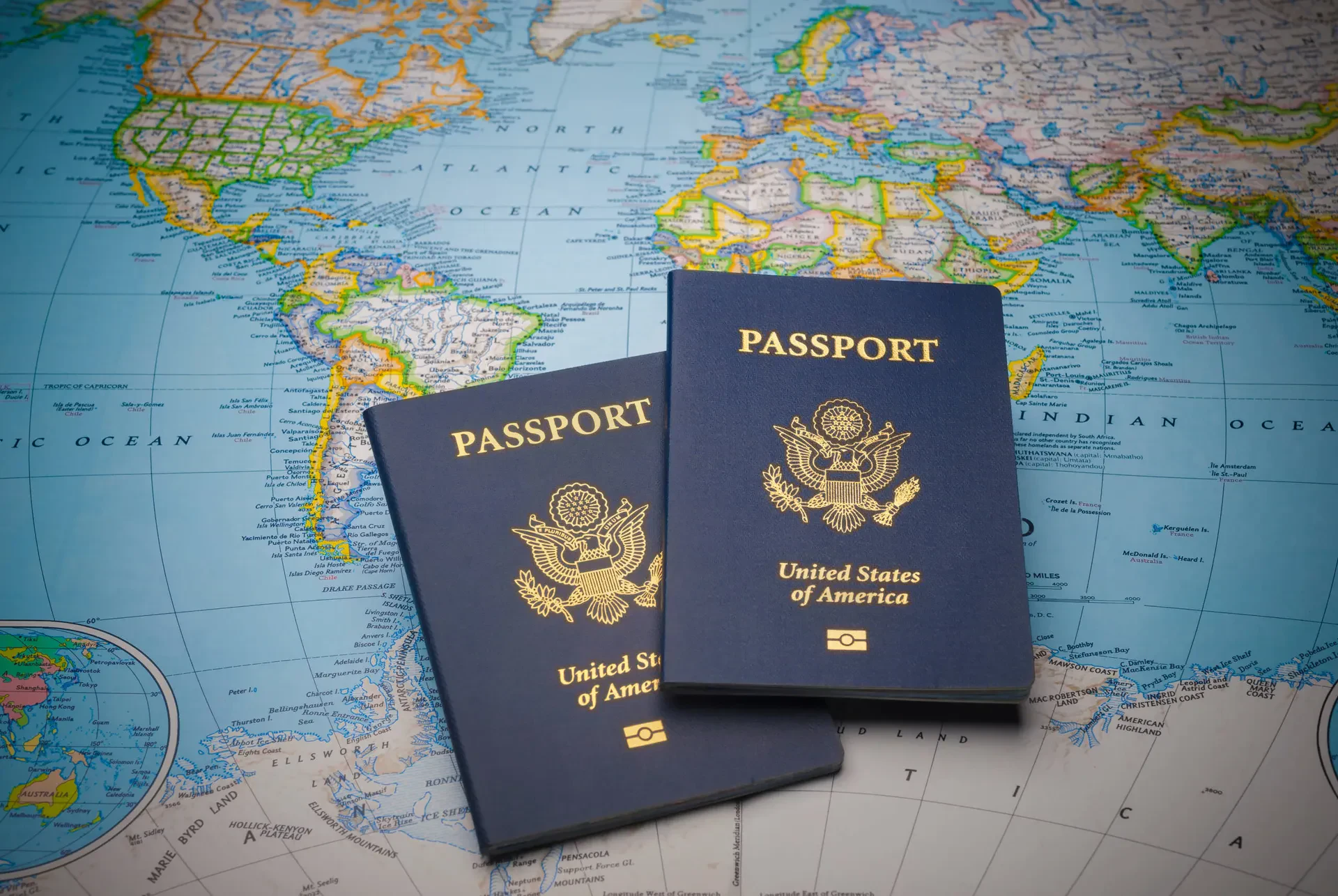 Two United States of America passports with dark blue covers and gold embossed seals rest on top of a colorful world map.