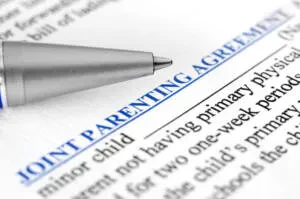 An elegant close-up shot of a silver ballpoint pen pointing toward a legal document titled "JOINT PARENTING AGREEMENT"