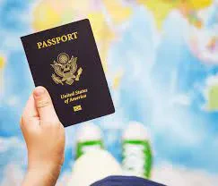 A top-down view of a young child's hand holding an official United States of America passport over a blurred world map background.