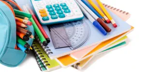 A collection of school supplies including notebooks, pens, and a calculator arranged on a wooden desk.