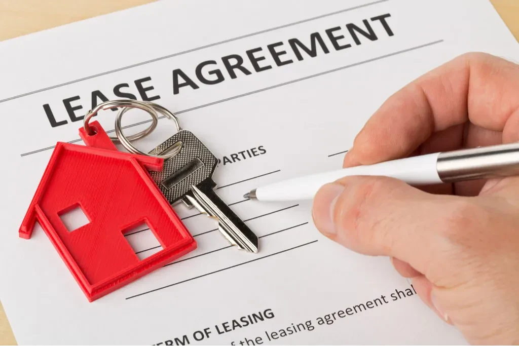 A close-up shot of a person's hand holding a white pen, poised to sign a document titled "LEASE AGREEMENT".