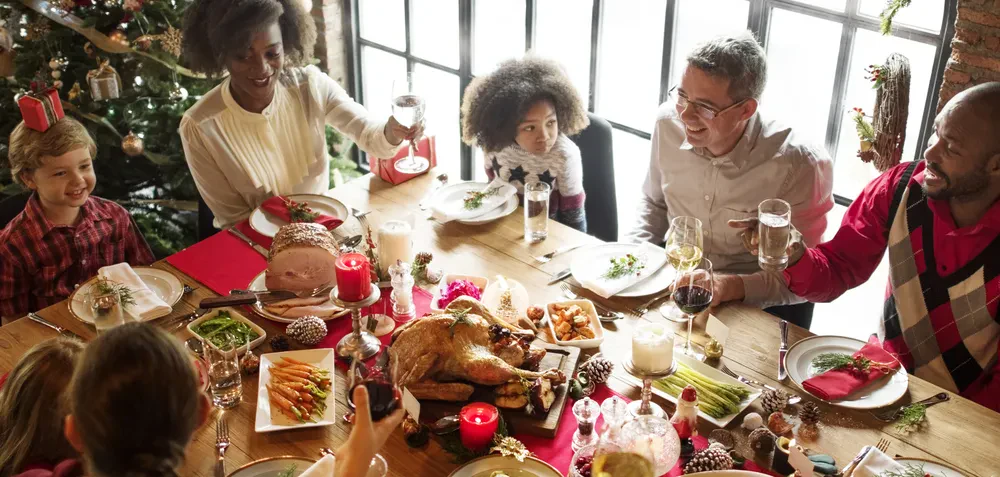 A family joyfully gathers around a table, sharing a festive Christmas dinner with food and decorations.