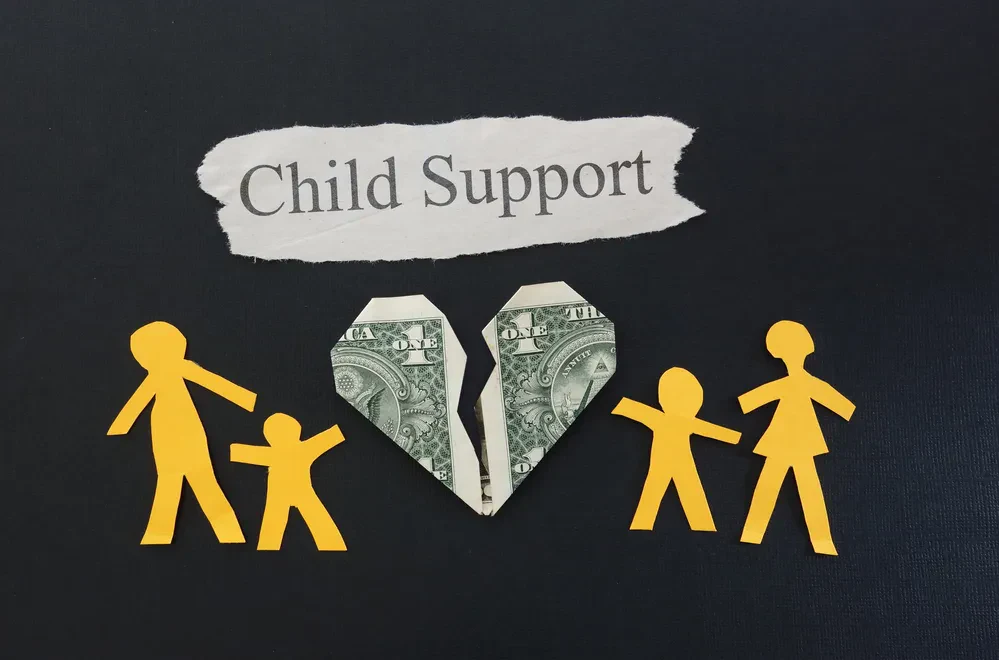 Paper cutouts of a family alongside a dollar bill, symbolizing the concept of child support and financial responsibility.