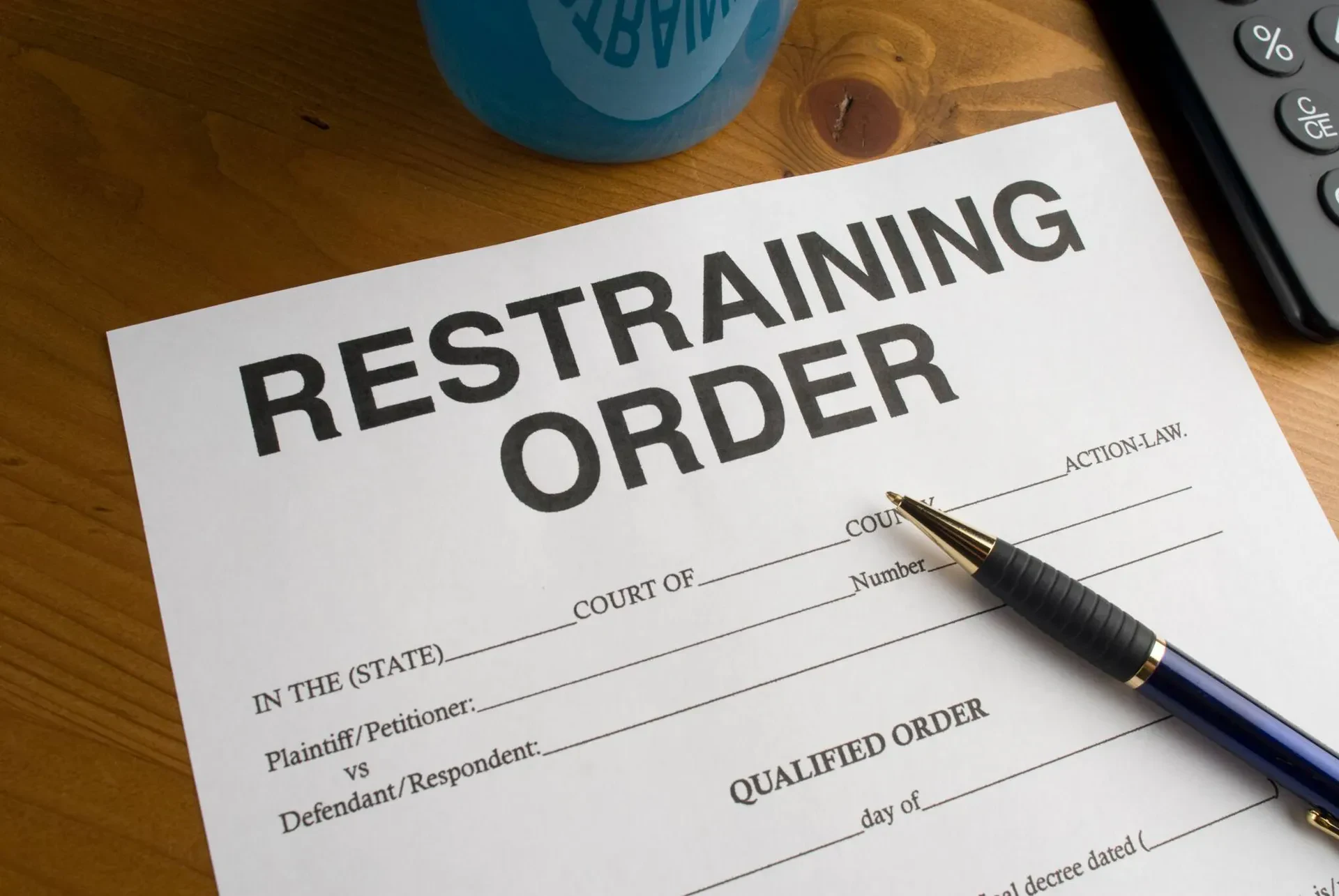 A restraining order form on a desk with a pen placed on top, next to a blue mug and part of a black phone visible.
