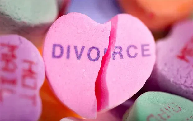 A pink heart-shaped candy with the word DIVORCE printed on it is shown cracked in half, surrounded by other pastel-colored candy hearts.