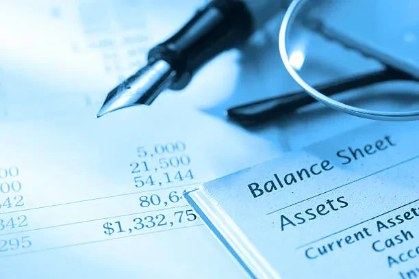 A balance sheet and a pen placed on a wooden desk, symbolizing financial analysis and planning.