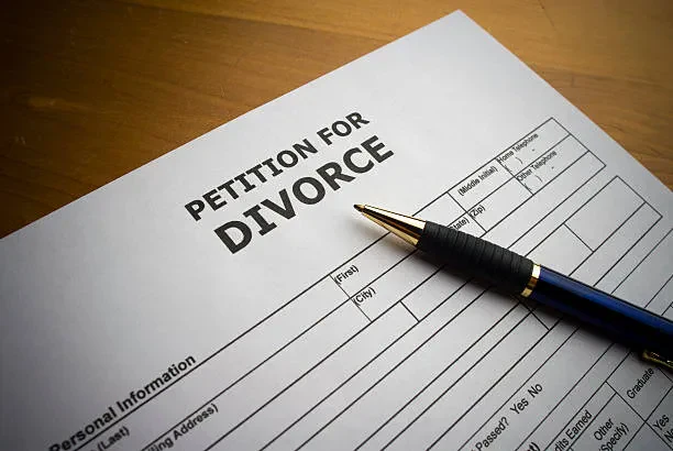 A close-up shot of a white "Petition for Divorce" legal document resting on a wooden surface, with a blue and gold pen lying diagonally across the form.