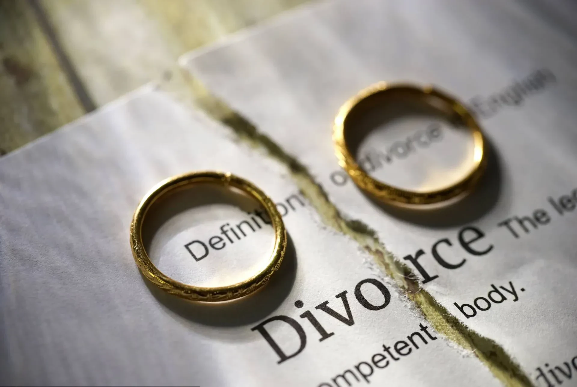 A torn document showing the definition of divorce, with two gold wedding rings separated by the tear.