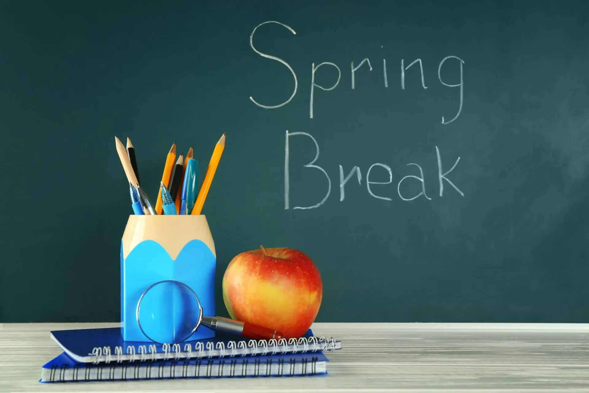 A collection of school supplies, including pencils and notebooks, alongside a red apple on a blackboard background.