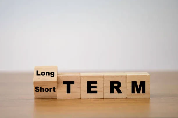 A photo of wooden building blocks spelling out "TERM" with a flippable block on the left showing both "Long" and "Short".