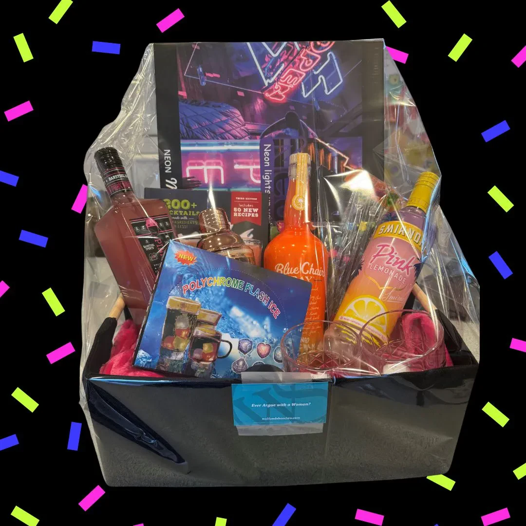 A gift basket filled with items like mugs, snacks, and bottles, wrapped in clear plastic cellophane and set against a blurry, warm light background.