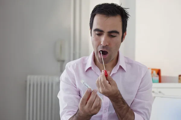 A man in a pink collared shirt performs a self-swab medical test inside his mouth.