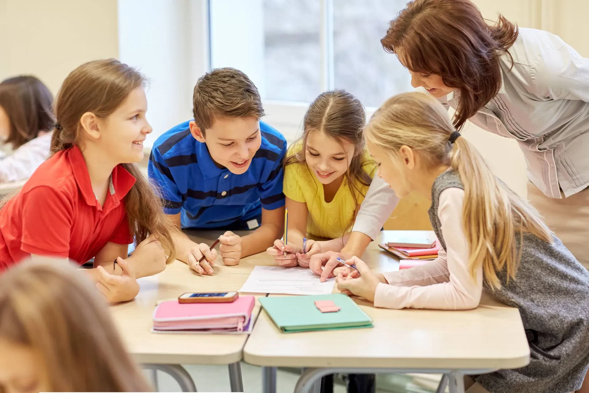A teacher and a group of children collaborate on a project, engaging in discussion and hands-on activities.