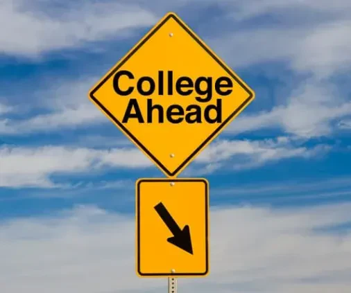 Yellow road sign reads College Ahead with a downward arrow below it, set against a blue sky with white clouds.