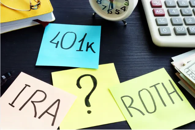 Sticky notes reading “401k,” “IRA,” “ROTH,” and a question mark are on a desk with a clock, calculator, notebook, and paper money, suggesting questions about retirement savings options.