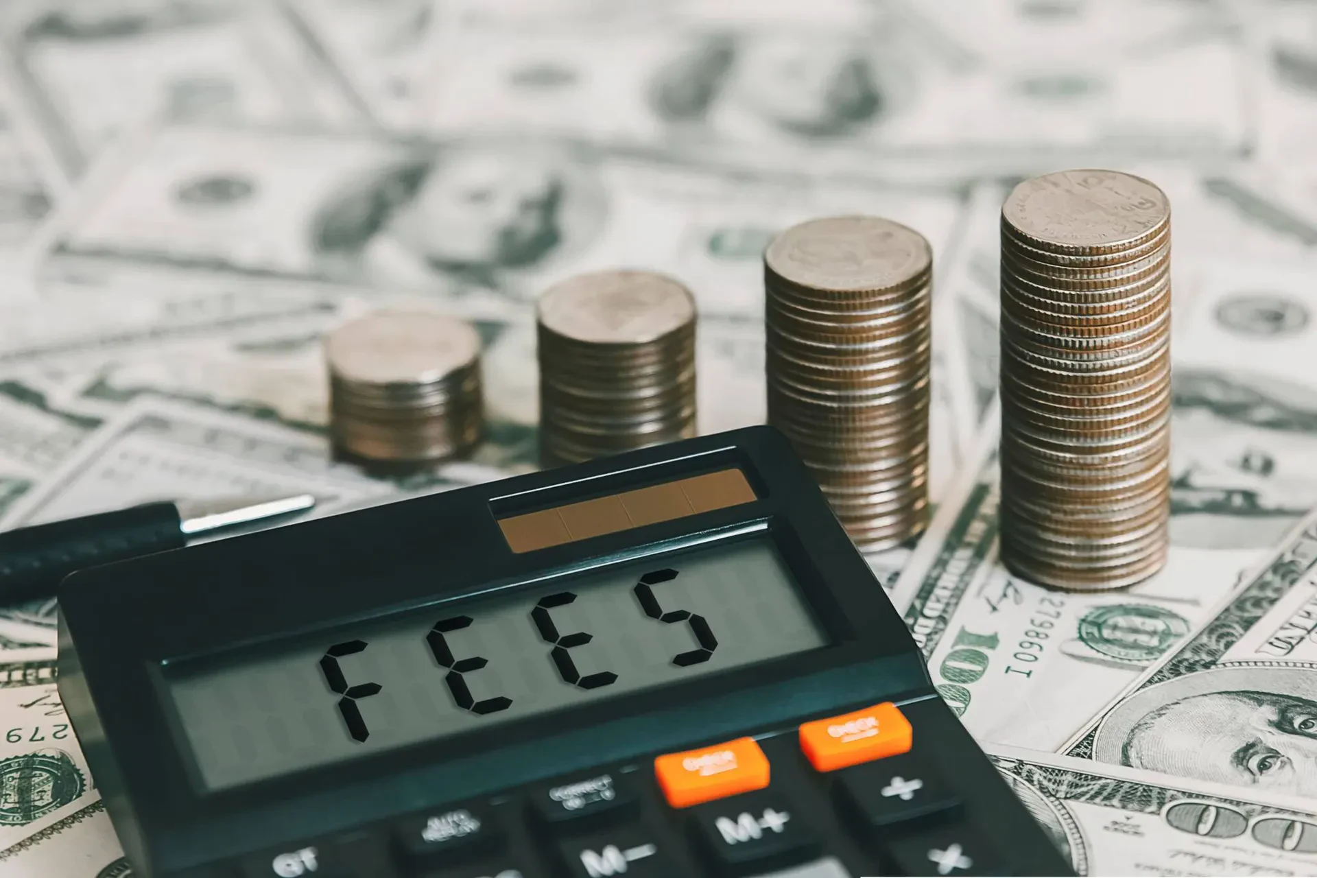 A black calculator displaying the word "FEES" upside down as "5337" sits in the foreground on a bed of US dollar bills.