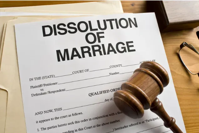 An overhead shot of a white "Dissolution of Marriage" document resting on a wooden desk alongside folders, a pair of eyeglasses, and a wooden judge's gavel.