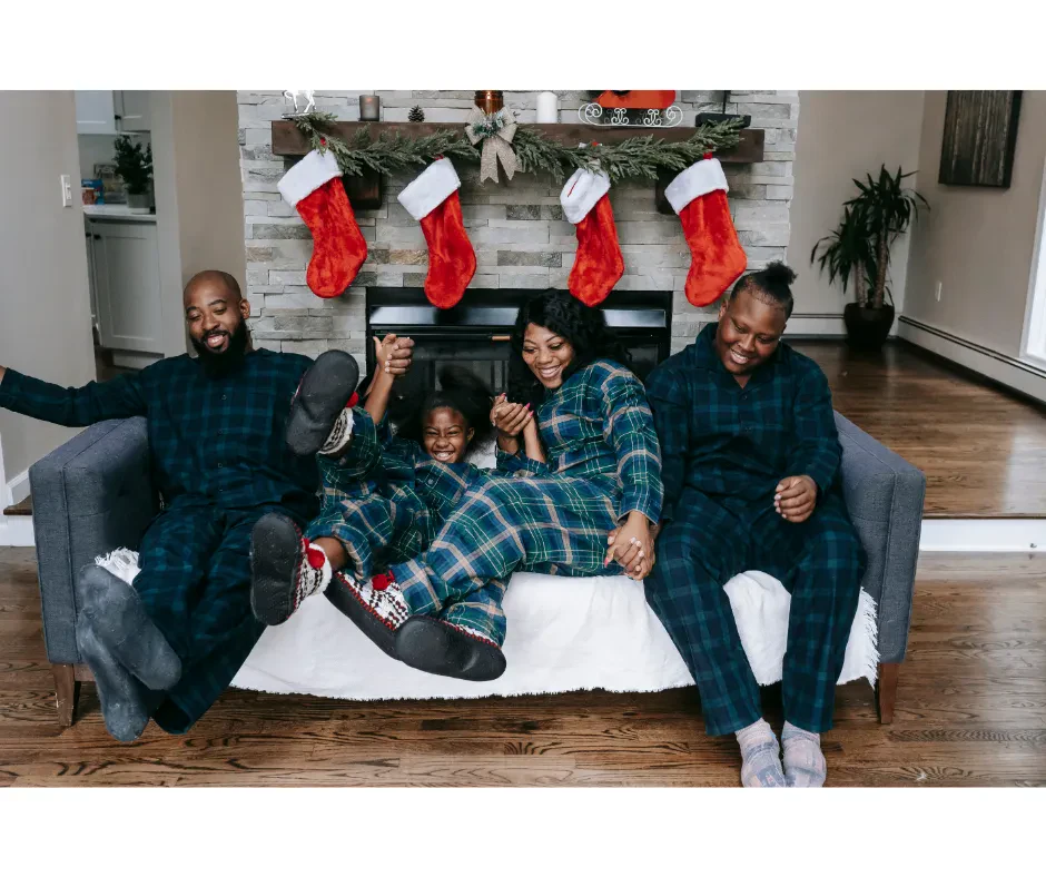A cheerful family of four in coordinated pajamas, sitting closely on a couch, enjoying a cozy moment together.