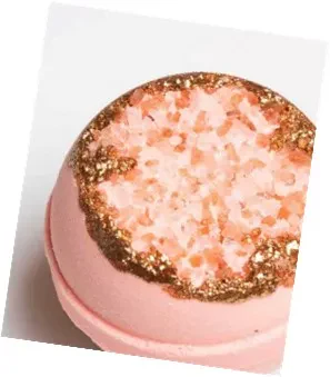 An image of a round, pink geode bath bomb with a textured top filled with light pink crystals, resembling a natural mineral crust, and bordered by a shimmering gold metallic rim.