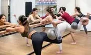 A group of women practicing yoga poses in a well-lit gym, focusing on balance and flexibility.
