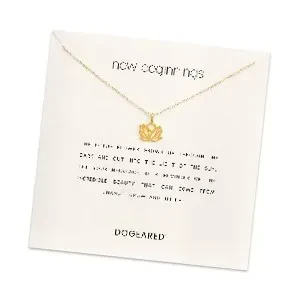 A gold delicate chain necklace featuring a lotus flower pendant, displayed on a square white card featuring the text "new beginnings" at the top and the brand name "DOGEARED" at the bottom.