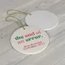 A flat-lay view of two circular white ceramic Christmas ornaments with gold hanging strings on a gray wood-textured surface.
