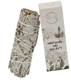 A white sage smudge stick bundled with white string, displayed next to its original white packaging box featuring a floral design of light roses and the bold text "clear him the f*ck out"