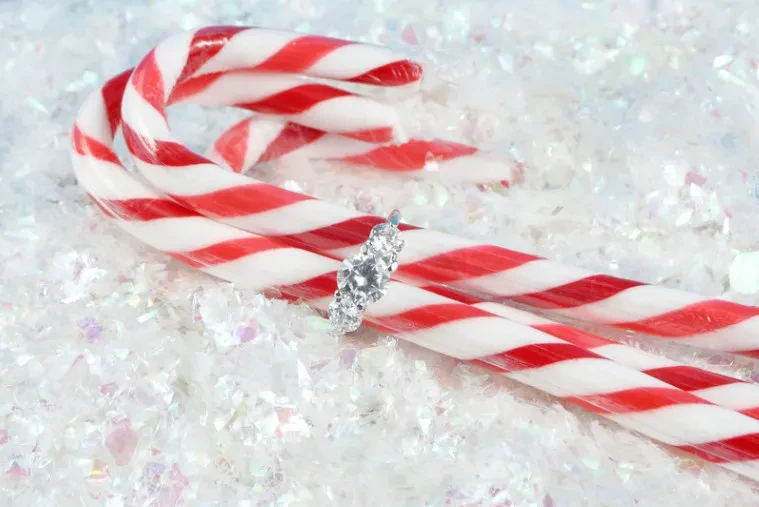 A candy cane topped with a sparkling diamond ring, symbolizing a festive engagement or celebration.